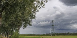Bewolkte lucht boven groene velden met windturbines en hoogspanningslijnen
