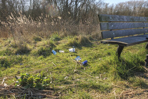 Litter scattered on the grass near a bench in a public park on a