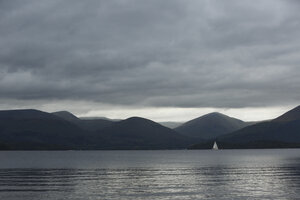 Zeilboot op bergmeer onder stormachtige hemel