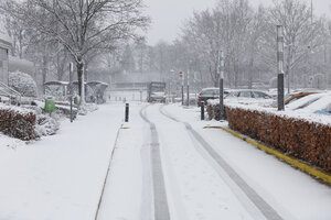 Besneeuwde straat met geparkeerde auto's en busbaan