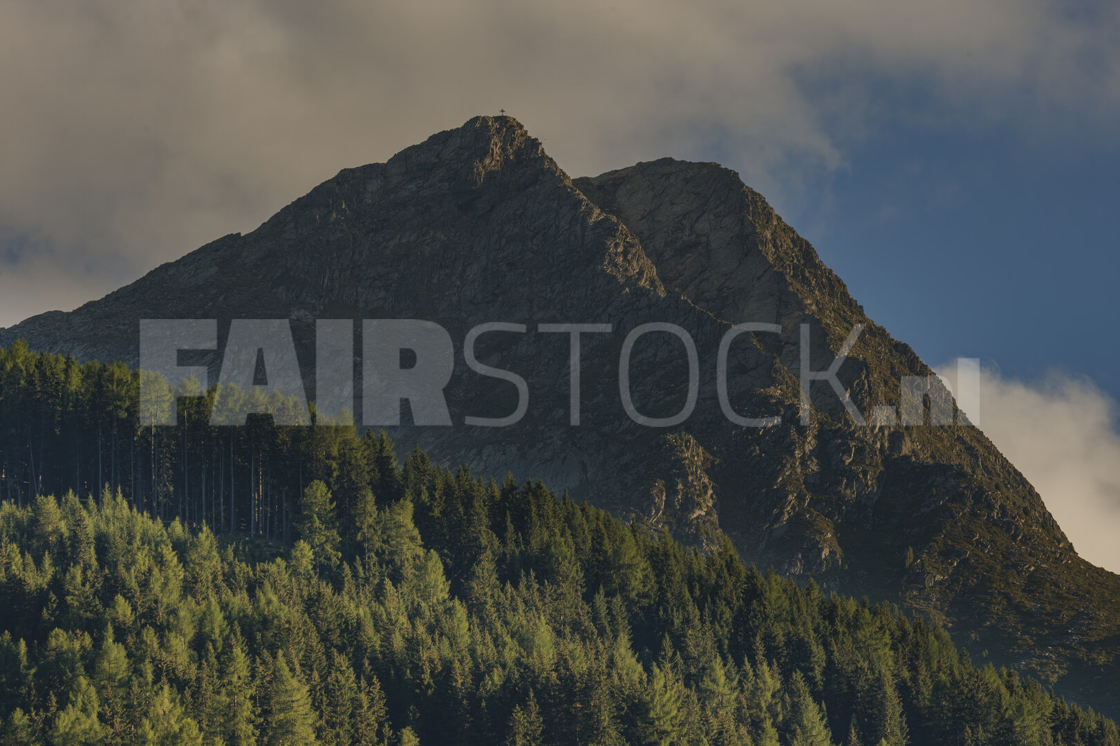 Oostenrijkse bergpiek met kruis boven dennenbos