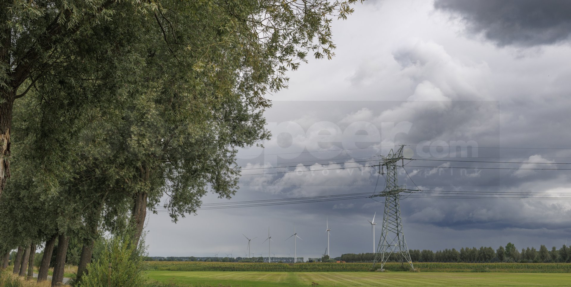 Bewolkte lucht boven groene velden met windturbines en hoogspanningslijnen