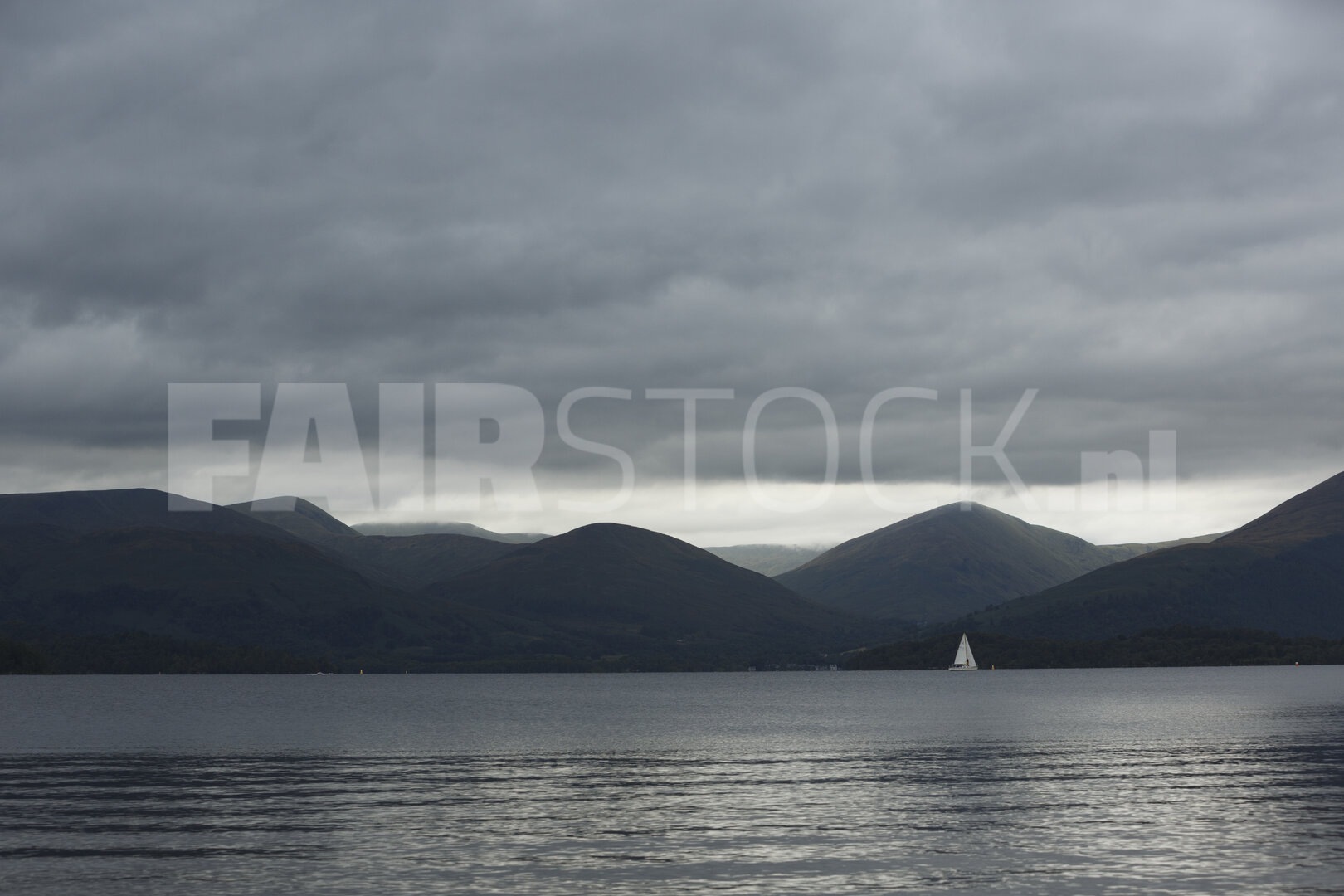 Zeilboot op bergmeer onder stormachtige hemel