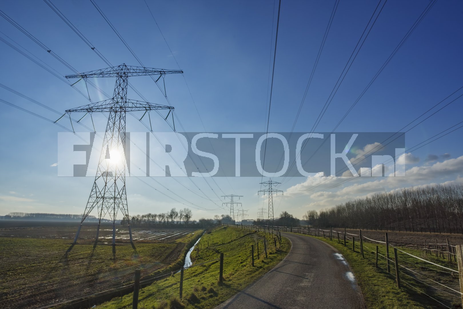 Hoogspanningslijnen in landelijk landschap onder blauwe lucht