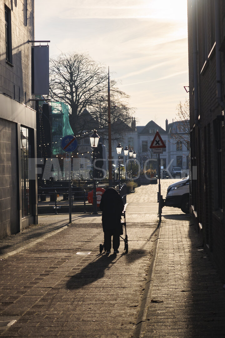Elderly woman walking with walker in quiet city street during go
