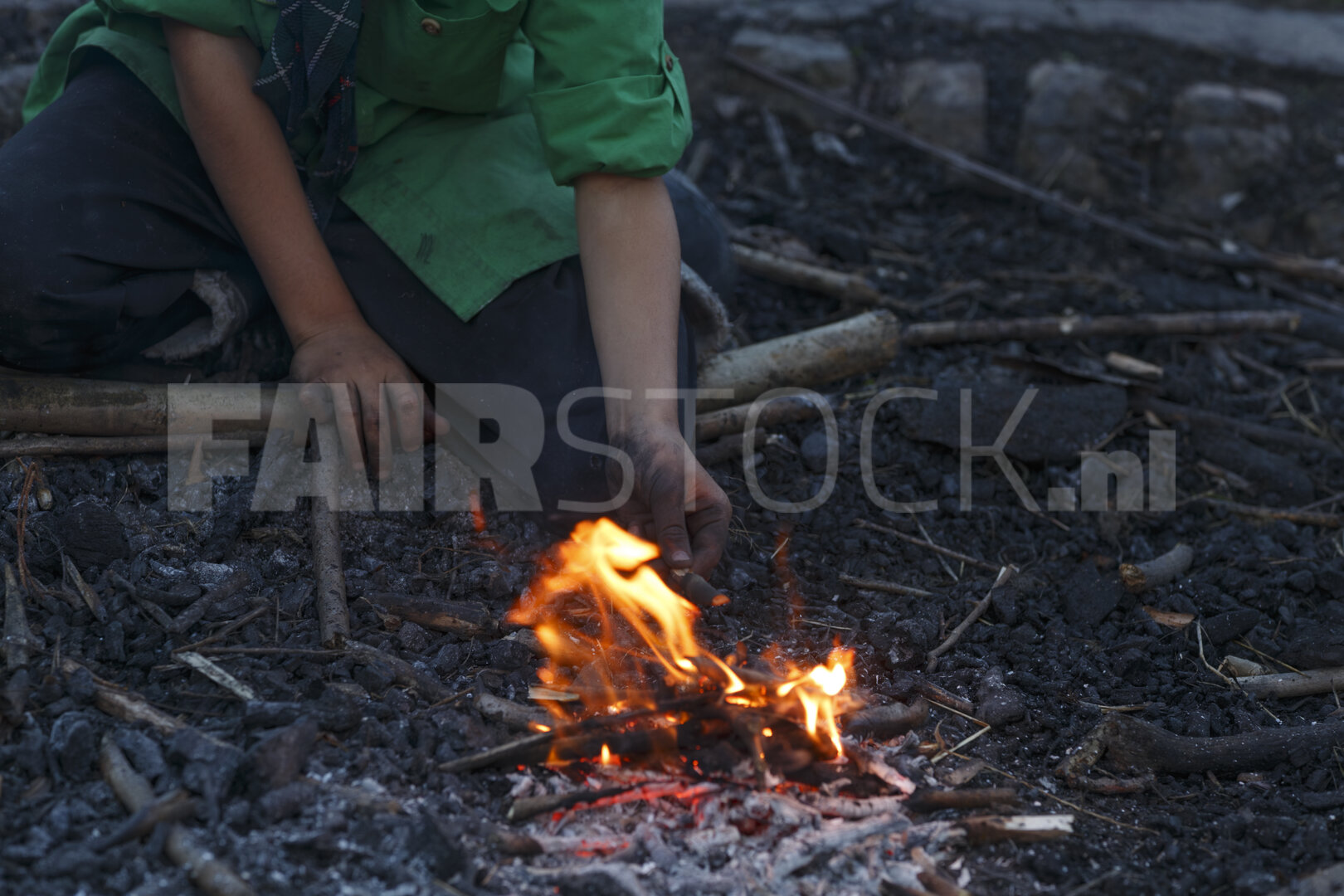 Persoon steekt vuur aan met takjes bij schemering